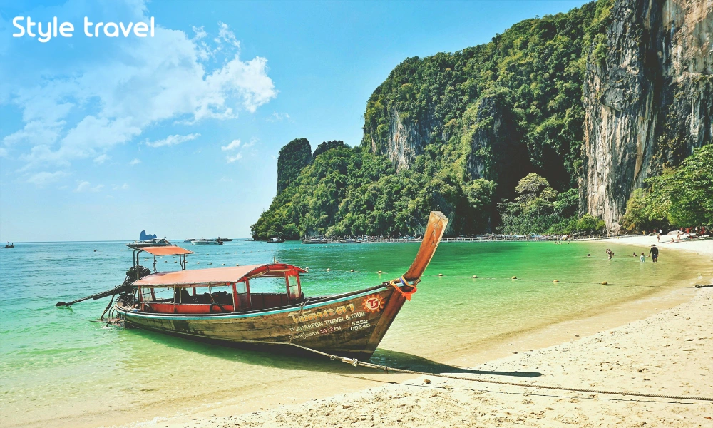 Longtail boat beside a sandy beach and limestone cliffs in Krabi